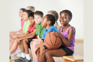 Smiling young children sitting on a sports bench with a little girl holding a basketball