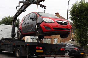 An abandoned red car being lifted onto a tow truck