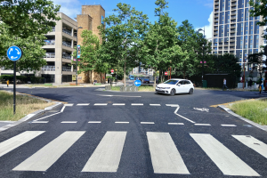 Newly-resurfaced road and zebra crossing on Dingwall Road, with a small white car travelling around the roundabout.