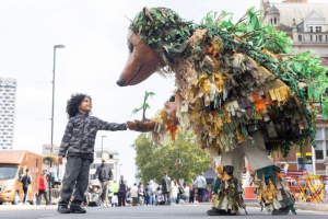 A person in a giant hedgehog costume greeting a young child outside Croydon Clocktower