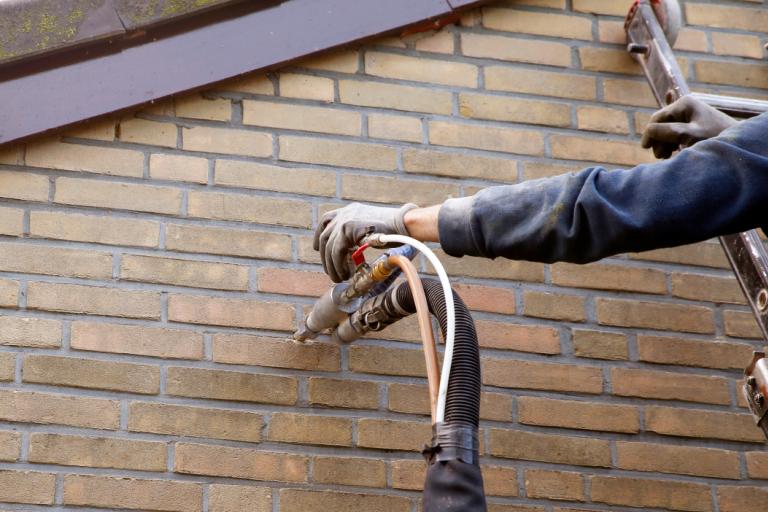 A man in protective clothing, installing insulation by injecting microbead pearls in the cavity walls