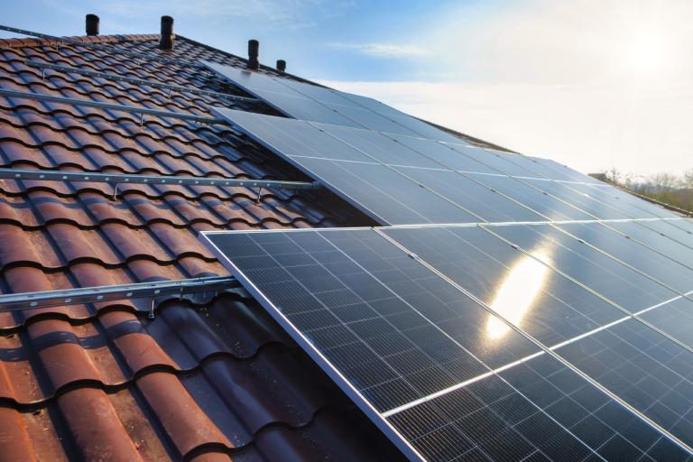 Installation of photovoltaic panels on a pitched roof with bright sunlight.