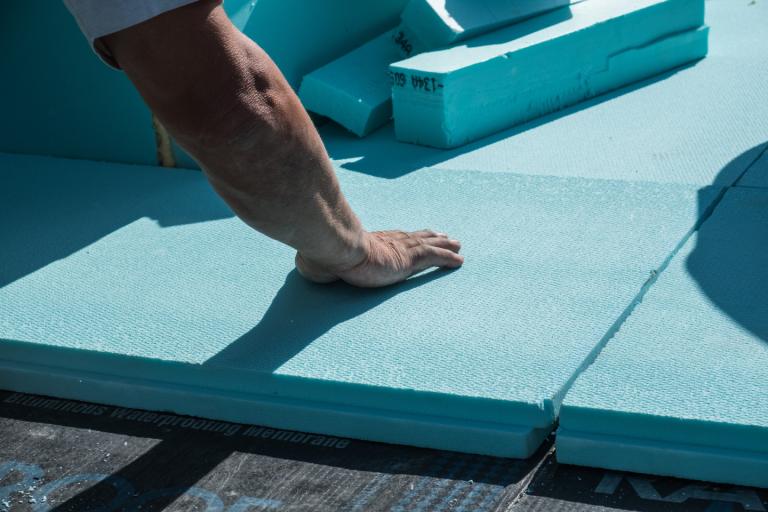 A roofer placing  energy saving XPS polystyrene insulation boards on a flat roof.